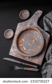 Empty wooden plate, knife, fork and cutting board set on textured concrete background - Shutterstock ID 2310730227