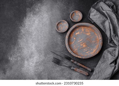 Empty wooden plate, knife, fork and cutting board set on textured concrete background - Shutterstock ID 2310730235