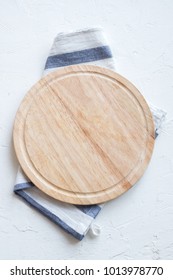 Empty Wooden Platter With Napkin On White Stone Table, Top View, Copy Space. Wooden Cutting Board Over White Concrete Background.