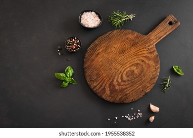 Empty Wooden Round Board With Herbs And Spices On Black Stone Kitchen Table, Top View, Flat Lay. Wooden Pizza Platter, Copy Space. Food Background.