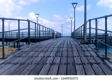 Empty Wooden Sea Pier With Street Lamps And The Pale Blue Cloudy Sky Above In Twilight 