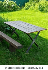 An empty wooden table and bench set placed on a lush green grass lawn.