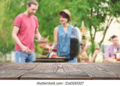 Empty wooden table and blurred view of people having barbecue with modern grill outdoors - Powered by Shutterstock