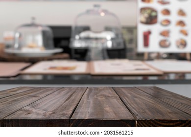 Empty Wooden Table With Blurry Background Of Cafe And Bakery Shop. There Is Sample Of Cake In Transparent Box. Can Be Used For Montage Or Display Your Products.