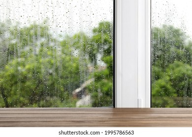 Empty wooden table near window on rainy day. Space for text