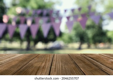 Empty Wooden Table In Park Decorated With Bunting Flags, Space For Design. Outdoor Party