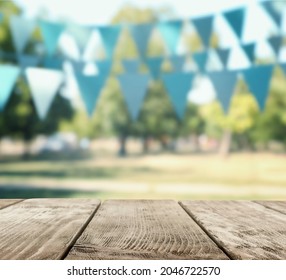 Empty Wooden Table In Park Decorated With Bunting Flags, Space For Design. Outdoor Party