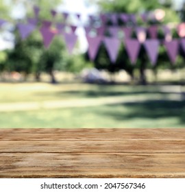 Empty Wooden Table In Park Decorated With Bunting Flags, Space For Design. Outdoor Party