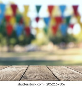 Empty Wooden Table In Park Decorated With Bunting Flags, Space For Design. Outdoor Party