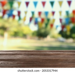 Empty Wooden Table In Park Decorated With Bunting Flags, Space For Design. Outdoor Party