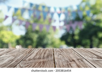 Empty Wooden Table In Park Decorated With Bunting Flags, Space For Design. Outdoor Party