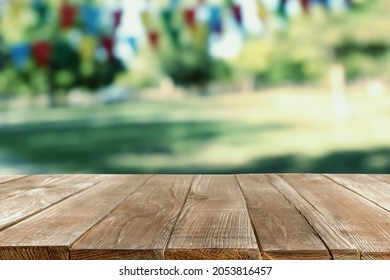 Empty Wooden Table In Park Decorated With Bunting Flags, Space For Design. Outdoor Party