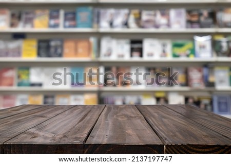 Empty wooden table platform and blurred background of library or book store setting with books and reading material. Can be used for montage or display your products.