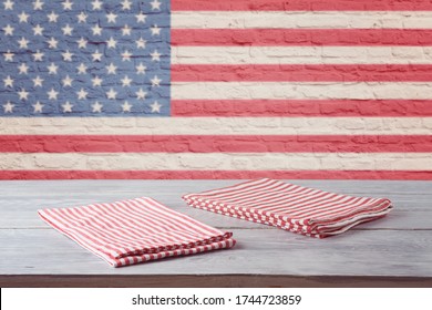 Empty wooden table with striped tablecloth over brick wall with american flag. 4th of july USA independence day mock up for design.