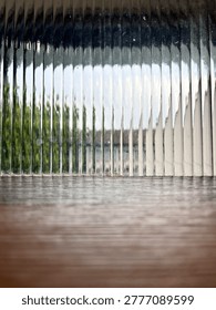 Empty wooden table surface with fluted glass background and blurred outdoor greenery view