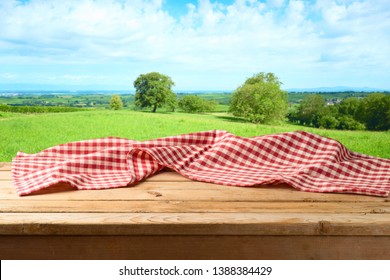 Empty wooden table with tablecloth over summer meadow background 