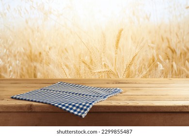 Empty wooden table with tablecloth over wheat field blurred background. Shavuot holiday mock up for design and product display