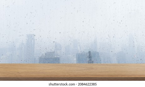 Empty Wooden Table Top In Foreground With Wet Transparent Window Glass, Highrise Buildings View On Background. Counter Bar Foreground Can Be Used For Display Or Montage Products. 