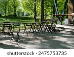 Empty wooden tables and chairs in a street eatery. An open-air cafe in a quiet city green park on an early sunny morning without people