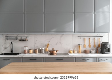 Empty wooden tabletop in scandinavian style kitchen with gray furniture. Countertop with various jars and tableware in apartment with minimalist bright interior.