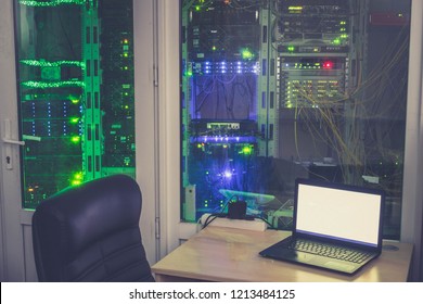 Empty workplace of the system administrator is in the server room. Many racks with computer equipment are behind the glass wall of a modern data center.  - Powered by Shutterstock