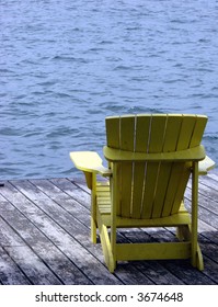 Empty Yellow Adirondack Chair On A Dock Over The Water