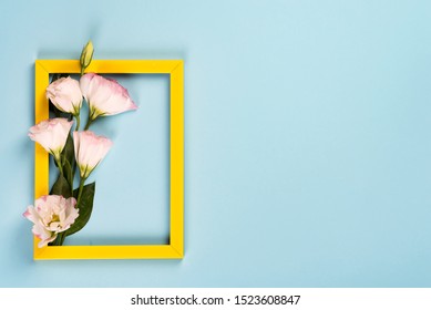 Empty yellow frame with flowers eustoma on blue paper background with copy space. Flat lay. Love concept