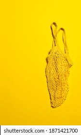 Empty Yellow Mesh Bag On Bright Yellow Paper Background. Flat Lay. Vertical Orientation. Conscious Consumerism And Eco Friendly Shopping Concept. Copy Space.