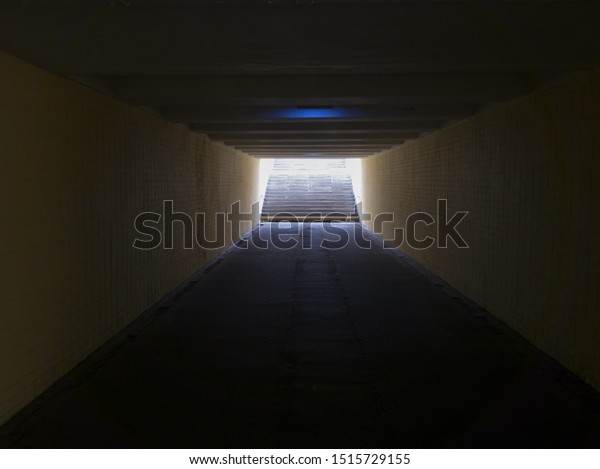 Empty\
yellow underground pedestrian crossing. Tunnel and daylight at the\
end. Steps to the top at the pedestrian crossing. A long concrete\
tunnel with lanterns in the city\
underground.