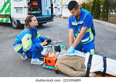 EMS, First Aid. Two Paramedics Performing Closed-chest Cardiac Massage For Victim Man Who Lies Unconscious On Medical Stretcher Near Ambulance Outdoor