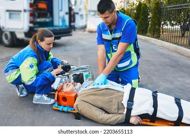 EMS Paramedics Performing Closed-chest Cardiac Massage And Artificial Respiration For Injured Mature Man Who Lies Unconscious On Medical Stretcher Near Ambulance Outdoor