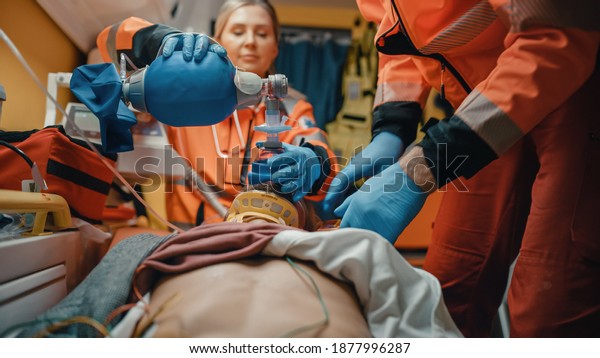 EMS\
Paramedics Team Provide Medical Help to Injured Patient on the Way\
to Hospital. Emergency Care Assistants Using a Ventilation Mask to\
Bring the Man Back to Life in an\
Ambulance.