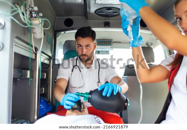 EMS Paramedics Team Provide Medical Help to\
Injured Patient on the Way to Healthcare Hospital. Emergency Care\
Assistant Using Ventilation Mask in an Ambulance. Young female\
nurse holding iv solution