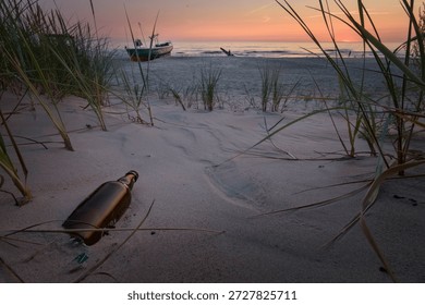 an emtpy bottle with no message stranded in the sand with beach, boat and sunset background