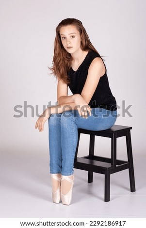 En Pointe resting on stool legs together unemotional en pointe Beautiful teen girl sitting straight looking at the camera, head tilted with an intimate straight gaze. Metaphor for trouble and secrets.