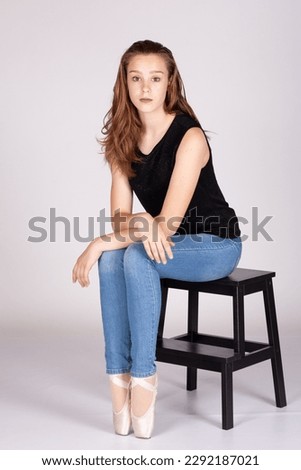 En Pointe resting on stool legs together unemotional en pointe Beautiful teen girl sitting straight looking at the camera, hand to chin with an intimate straight gaze. Metaphor for trouble or secrets.