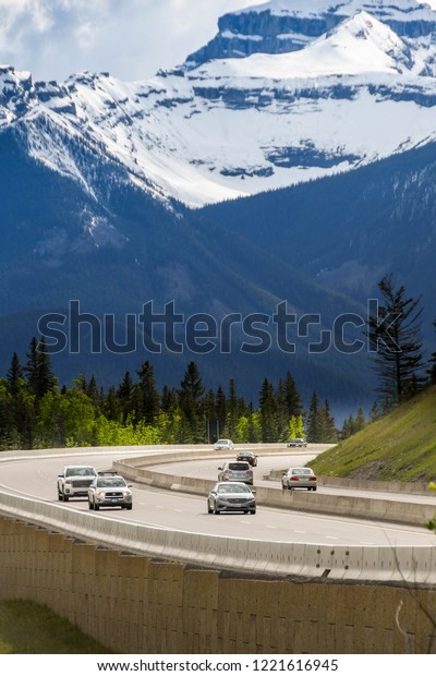 EN ROUTE REVELSTOKE TO LAKE\
LOUISE, AB - JUNE 2018: Cars and trucks passing snow capped\
mountains on the Trans Canada Highway approaching Lake Louise,\
AB.