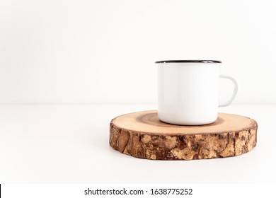 Enamel mug mock up with wooden cut tree section on a white table. Boho design of tin cup on white background with copy space for image or text