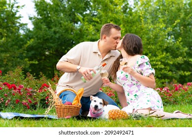 Enamored Woman And Man Kissing, Holding Glasses Of Wine, Walking The Dog. Romantic Family, Couple In The Garden On Picnic Kissing