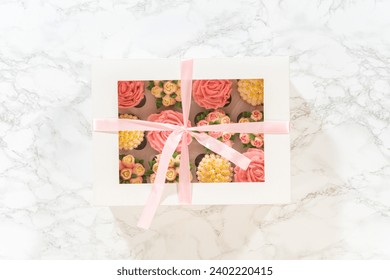 Encased in a pristine white paper cupcake box, each gourmet cupcake is a work of art, adorned with buttercream frosting flowers beautifully designed to resemble vibrant roses and tulips. - Powered by Shutterstock