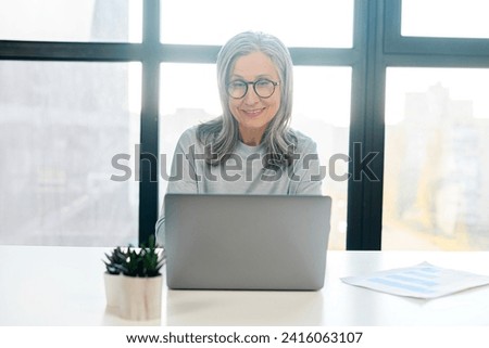 Enchanting mature businesswoman wearing stylish eyeglasses and smart casual wear using a laptop for office work, female employee checks mail, conducts business correspondence with customers