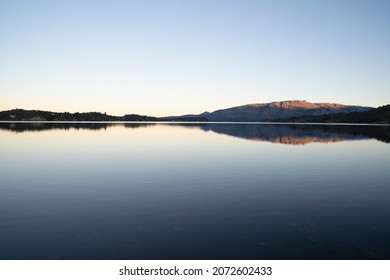 Enchanting view of the placid lake at sunset. The mountains, forest and blue sky reflection in the water.  - Powered by Shutterstock