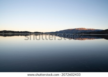 Enchanting view of the placid lake at sunset. The mountains, forest and blue sky reflection in the water. 