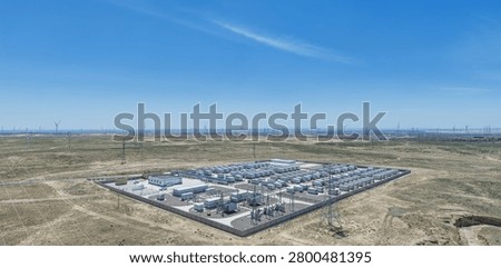 Enclosed battery container array with control buildings and switchgear, surrounded by transmission towers and distant wind turbines under a vast blue sky—typical utility-scale renewable integration site. Ningxia, China.
