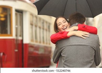 Encounter after a travel of a happy couple hugging in the street in a tram station in a rainy day under an umbrella - Powered by Shutterstock