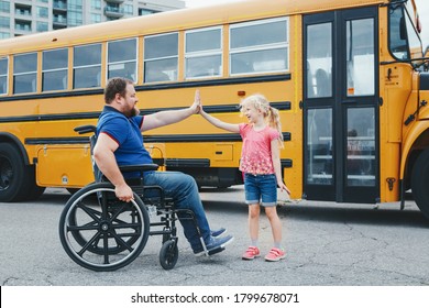 Encourage And Support From Family Members. Disabled Caucasian Father On Wheelchair With Daughter By Yellow School Bus. Back To School. High Five Gesture Between Dad And Kid.