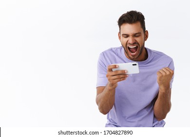 Encouraged satisfied handsome bearded man, triumphing as watching online video live stream of football game using smartphone, fist pump, winning arcade or race, passed hard level, smiling pleased
