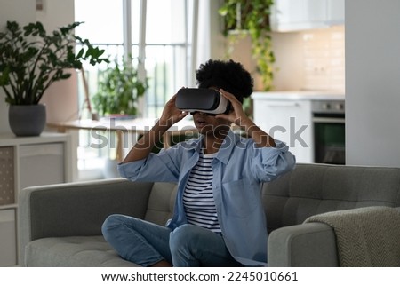 Encouraged surprised woman using VR glasses for first time to watch movies with 3D effect sits on sofa at home. Shocked horny girl using virtual reality helmet and opening mouth during surprise moment