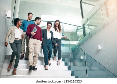 The end of another successful business day. Shot of a group of colleagues talking together while walking down stairs in a large modern office.