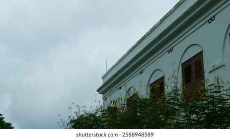 The end of the building captured in the low angle photograph shows trees that cover part of the building area.